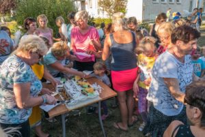 Trzy kobiety kroją i podają tort. Przy stoliku stoi kolejka dzieci i dorosłych.