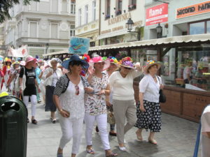 Duża grupa ludzi w ozdobnych kapeluszach, idzie po chodniku.